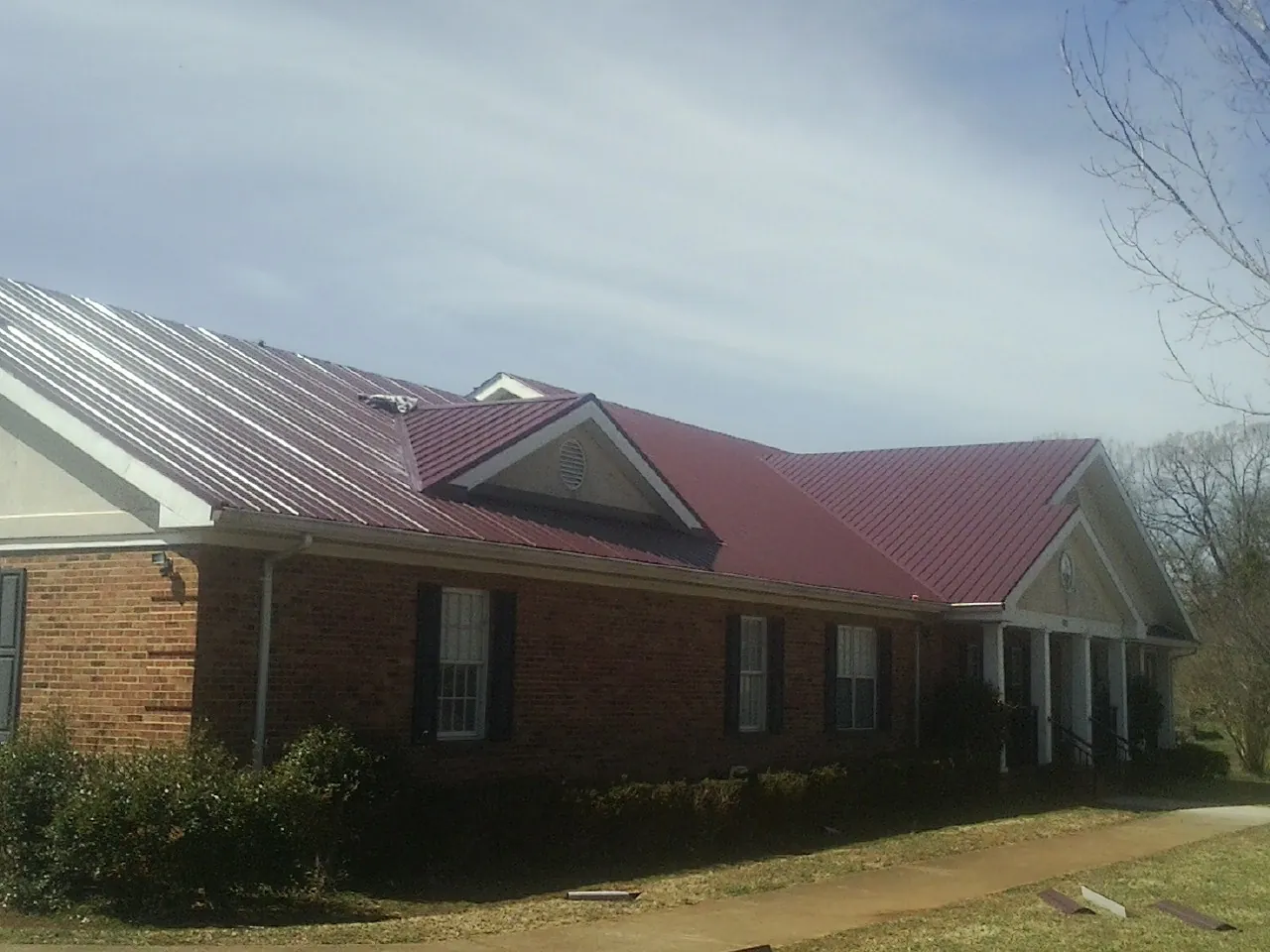 Red metal roof with gabled entries on a long brick building, from a Hail Damage Roof Repair job in Marco Island