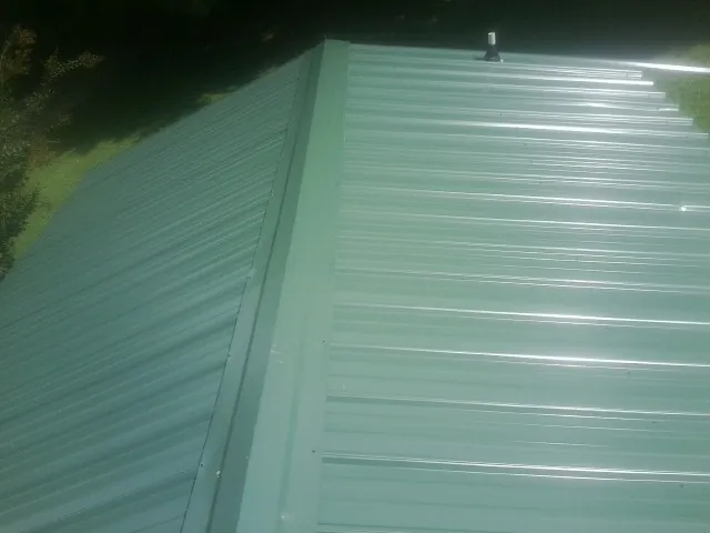 New green metal panels meeting at the ridge of a roof — Flat Roof Repair work by our crew in Marco Island