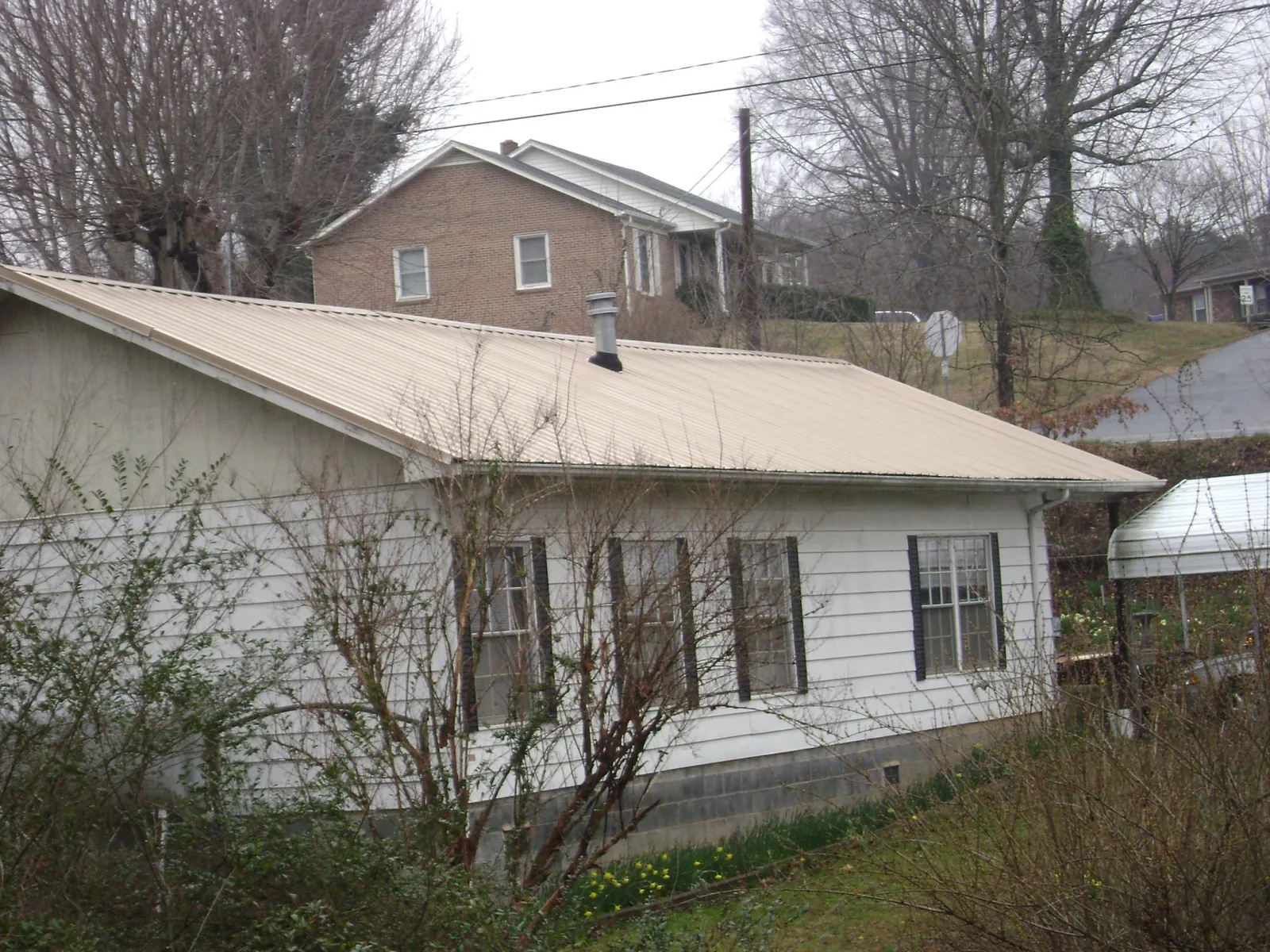 Tan metal roof on a white sided house set into a hillside — Commercial Roofing by Roofing Brothers in Marco Island